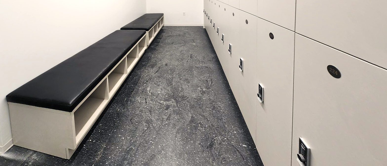 Black laminate fitness lockers with premium gym bench and stone floor — corporate wellness facility