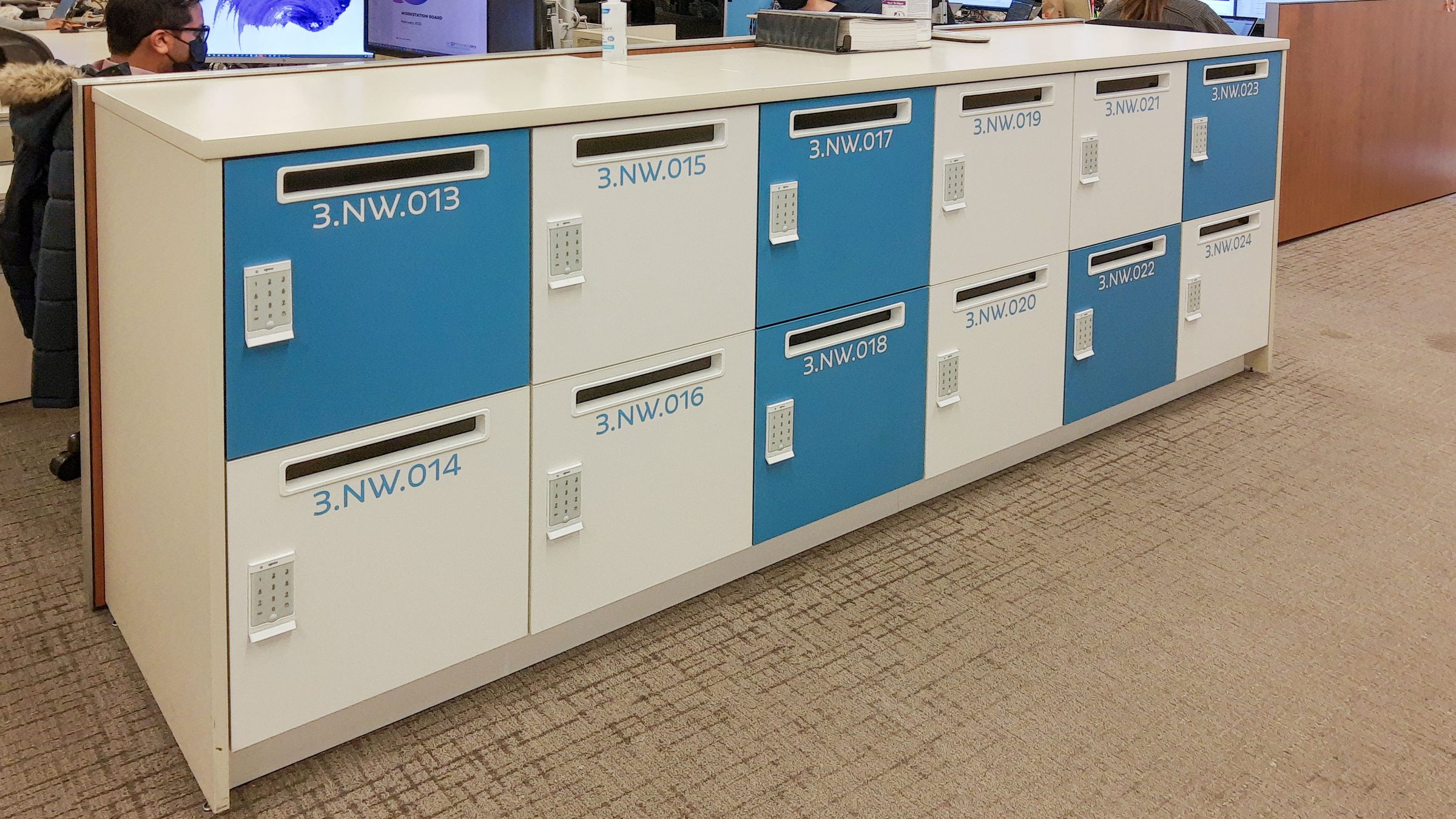 Blue branded locker island with mail slots in open office