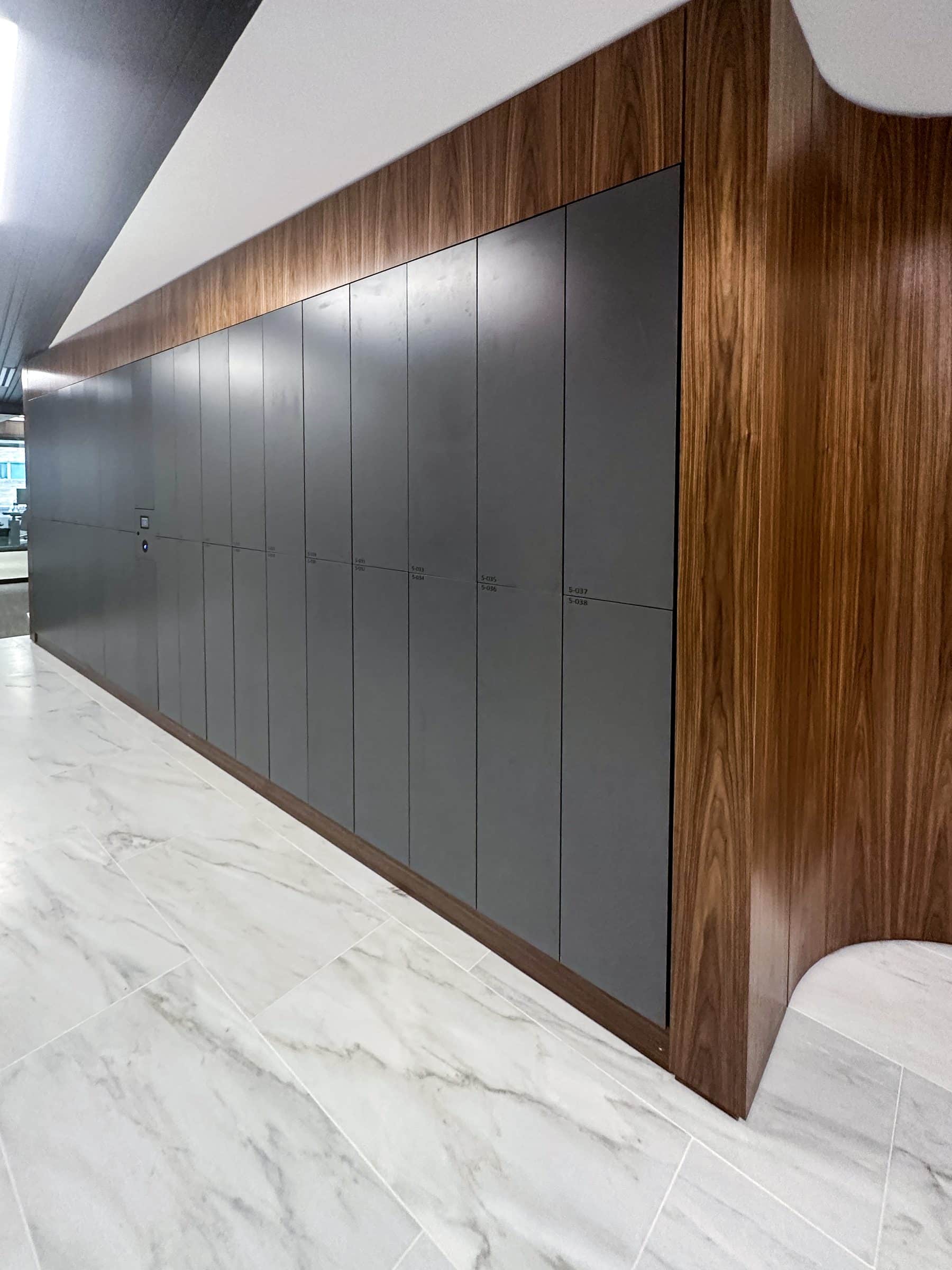 Charcoal lockers with walnut panels on marble floor — luxury NYC office
