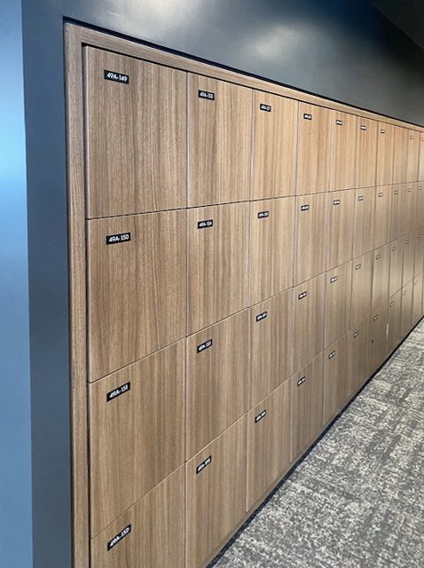 Dark oak 3-tier wall lockers in a corporate office corridor with dark accent wall
