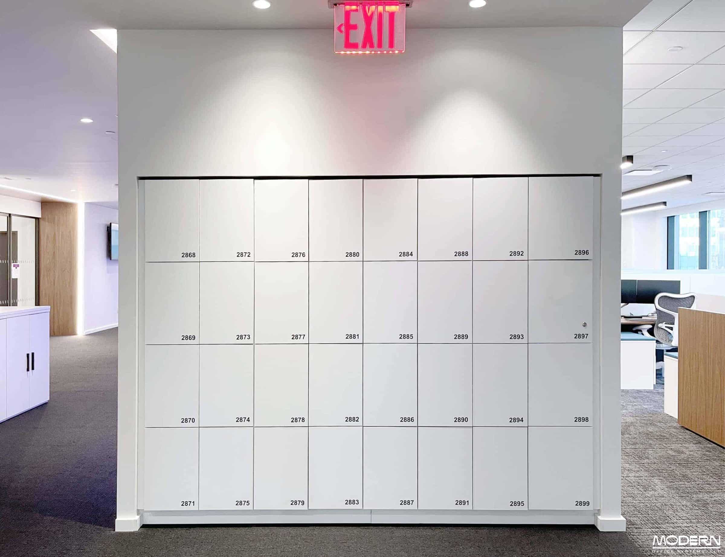 White 4-tier numbered wall locker bank in a large NYC open-plan corporate office — enterprise storage program